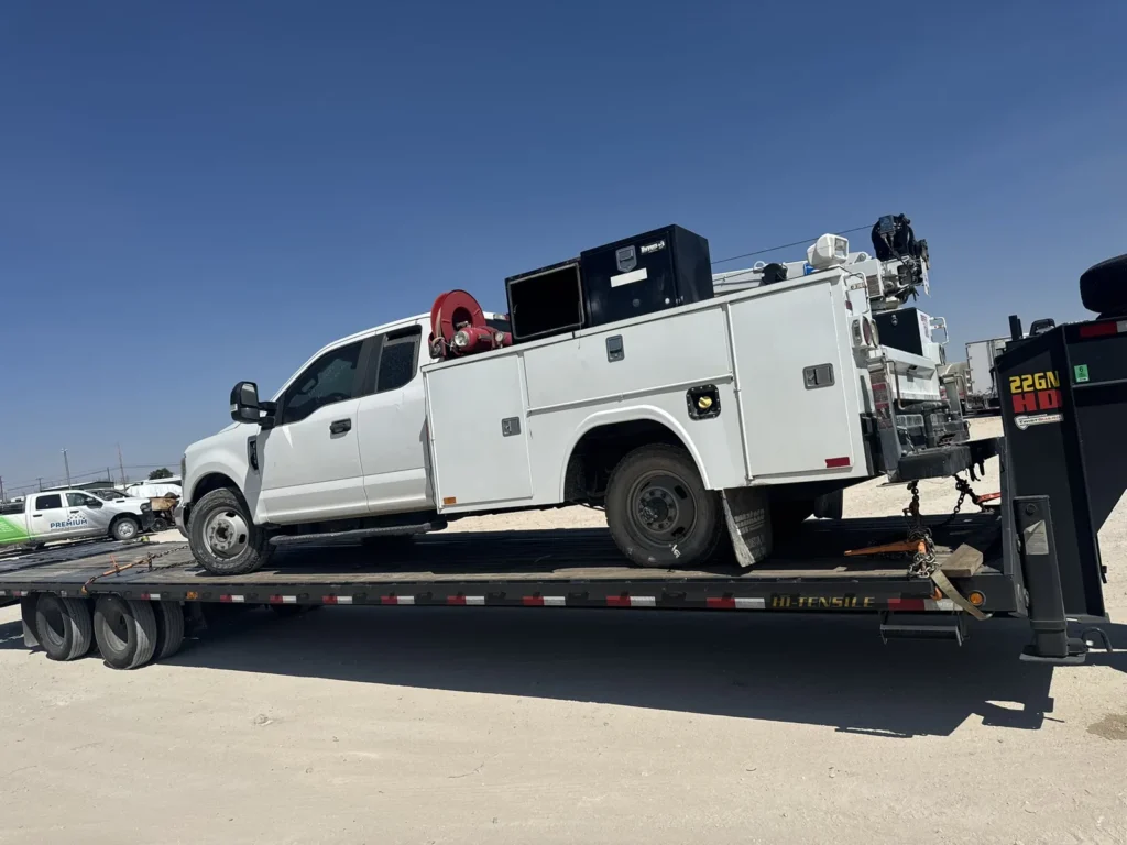 White service-body truck secured on a flatbed trailer under clear daylight