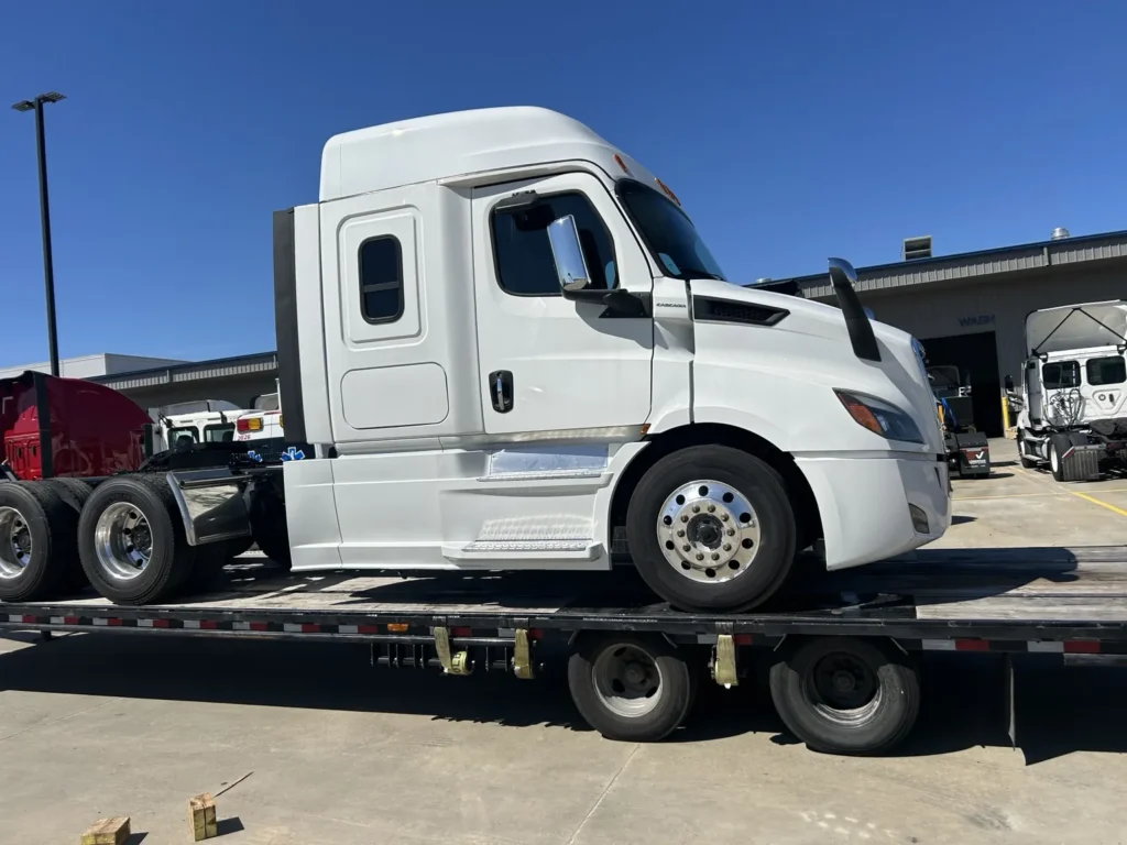 White sleeper tractor shown on a flatbed trailer in an equipment yard