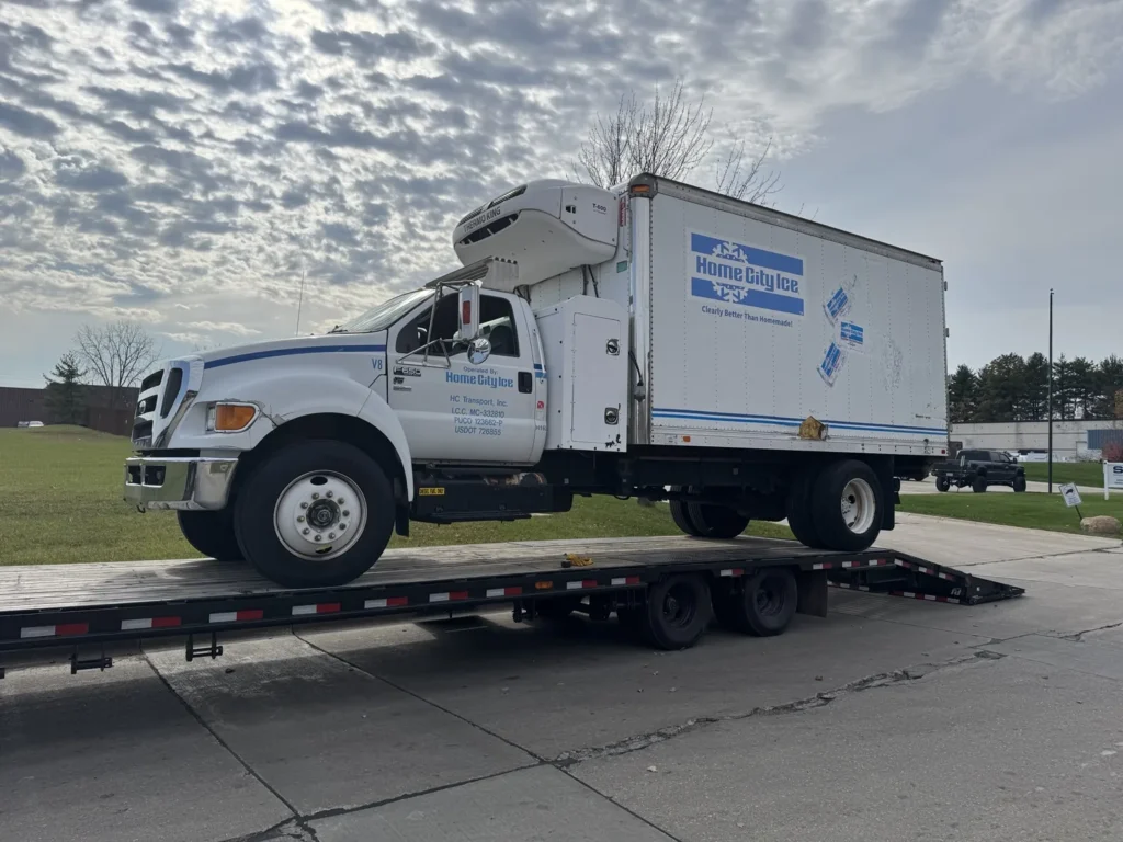 White medium-duty box truck positioned on a flatbed trailer