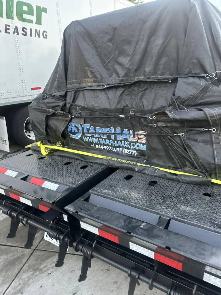 Covered freight on a flatbed with fitted black tarp and visible tie-down points