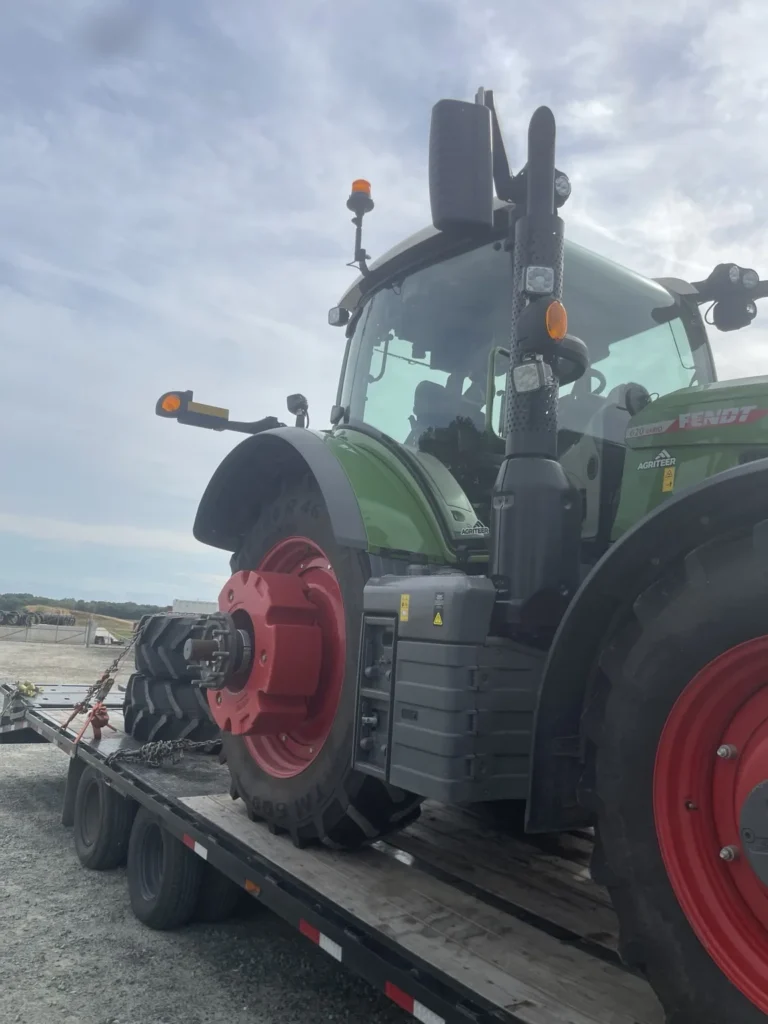 Large green agricultural tractor positioned on a flatbed with detached tire assemblies