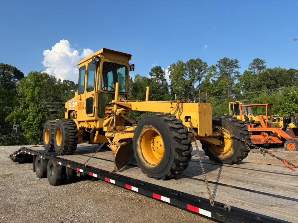 Large motor grader positioned lengthwise on a flatbed trailer