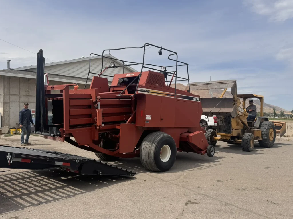 Large red agricultural machine positioned beside a loading ramp and support equipment