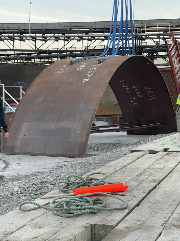 Large curved fabricated steel section staged for lifting and trailer placement