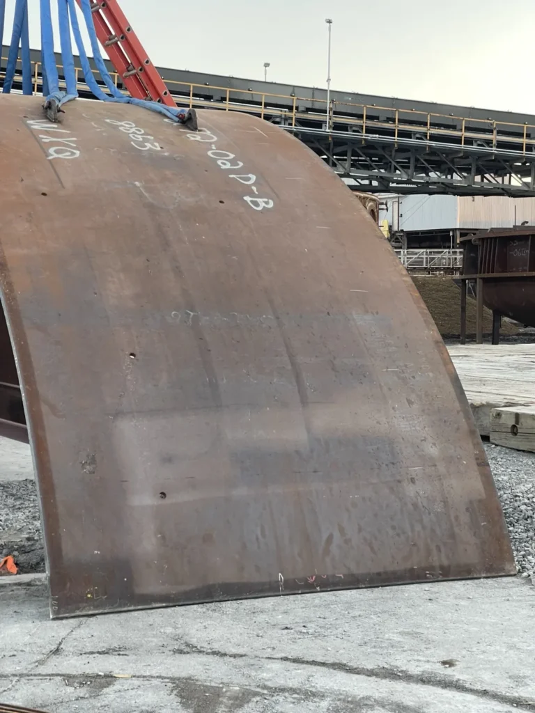 Large curved fabricated steel component shown during crane handling