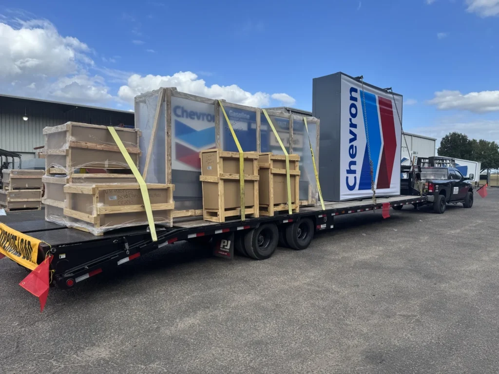 Crated and packaged materials arranged on a flatbed beside a commercial facility